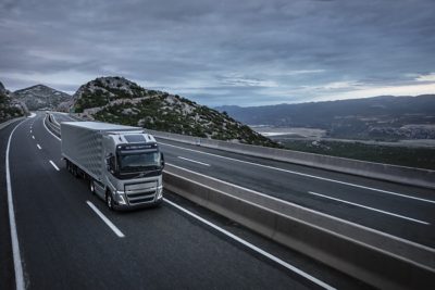 A truck drives over a bridge with mountains in the background