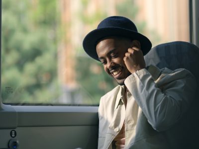 Ung smilende mann som sitter på en buss og snakker i mobiltelefonen.
