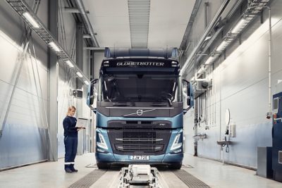 A Volvo service technician holds a computer as she stands next to a truck