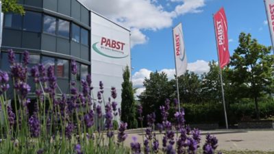 Ansicht des Verwaltungsgebäudes von Pabst Transport mit Firmenfahnen und blühendem Lavendel im Vordergrund bei sonnigem Wetter.