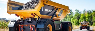 Two Volvo TA15 electric dumpers filled with crushed stone are driving on a road