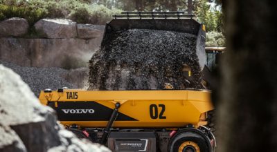 An excavator is loading crushed stone into a Volvo TA15
