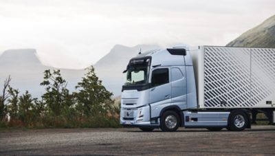 รถบรรทุกไฟฟ้า Volvo กำลังวิ่งบนถนนที่คดเคี้ยวผ่านภูมิประเทศชนบทใกล้แหล่งน้ำ