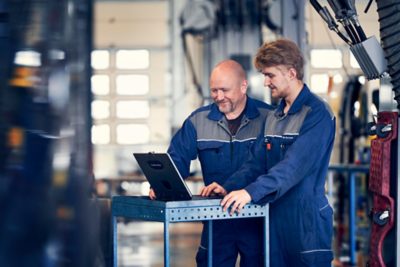 Dva mechanici Volvo při aktualizaci softwaru prostřednictvím notebooku v dílně