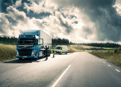Technik služby Volvo Action Service parkuje za nákladním vozidlem na kraji silnice. S řidičem nákladního vozidla na sebe mávají.