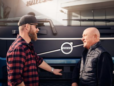 Two men speak in front of a Volvo truck