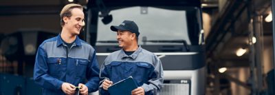 Two Volvo service technicians look at a laptop while standing next to a truck 