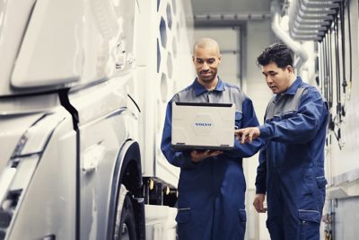 Two Volvo service technicians look at a laptop while standing next to a truck 