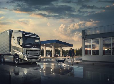 A driver and his dog walk in front of a Volvo truck parked at a gas station