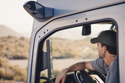 A driver and his dog walk in front of a Volvo truck parked at a gas station