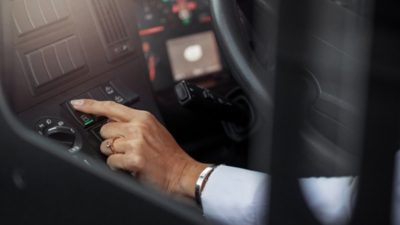 A bus driver’s left hand pushing a button in a Volvo bus dashboard