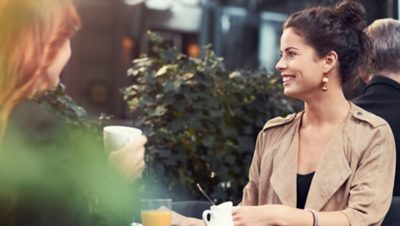 Two women having coffee at a calm bus stop in a city with Volvo’s quiet and clean electric city buses.