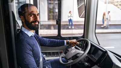 A smiling bus driver behind the steering wheel of a Volvo electric bus