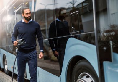 Un uomo con un cavo di ricarica si avvicina alla presa di ricarica di un autobus elettrico