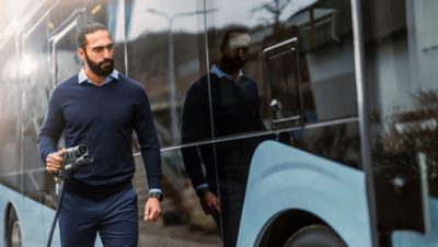 Un homme tenant un câble de charge s'approche de la prise de recharge d'un bus électrique