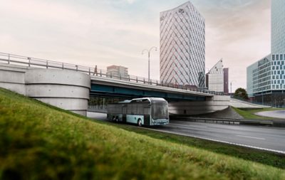 A Volvo 8900 Electric bus on the road on the outskirts of a modern city.