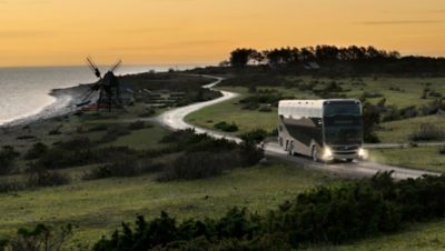 A Volvo 9700 DD driving on a seaside road in the sunset