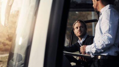 A bus driver behind the wheel of a Volvo 9700 DD in conversation with the on-board tourist guide