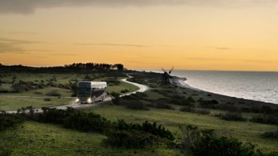 A Volvo 9700 Double Decker driving on a seaside road in the sunset