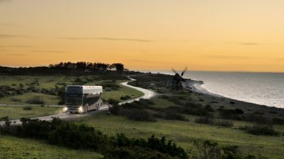 A Volvo 9700 Double Decker driving on a seaside road in the sunset