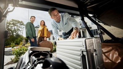 Driver unloading the luggage compartment of a Volvo 9700 coach with passengers waiting nearby