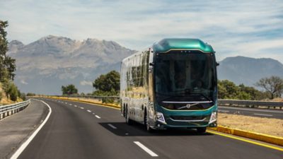 Front view of a Volvo 9800 driving on a motorway with mountains in the background.