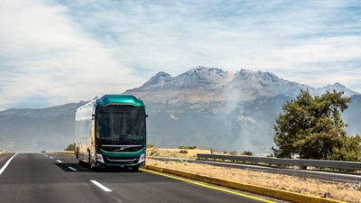 Front view of a Volvo 9800 on the road with mountains in the background 
