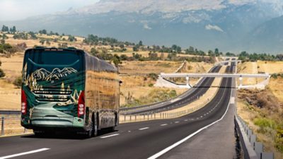 Rear view of a Volvo 9800 driving on a straight motorway through a rural landscape.