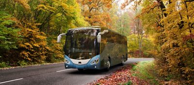 Blue coach on a road in the forest at autumn