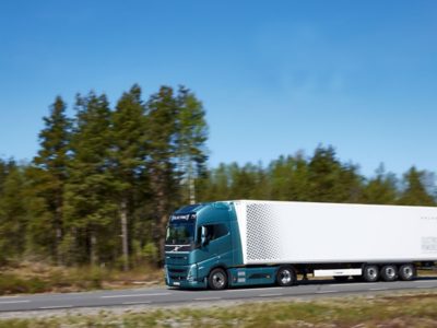 Volvo FH Electric ขับบนถนนที่มีต้นไม้อยู่ด้านหลังและท้องฟ้าสีคราม