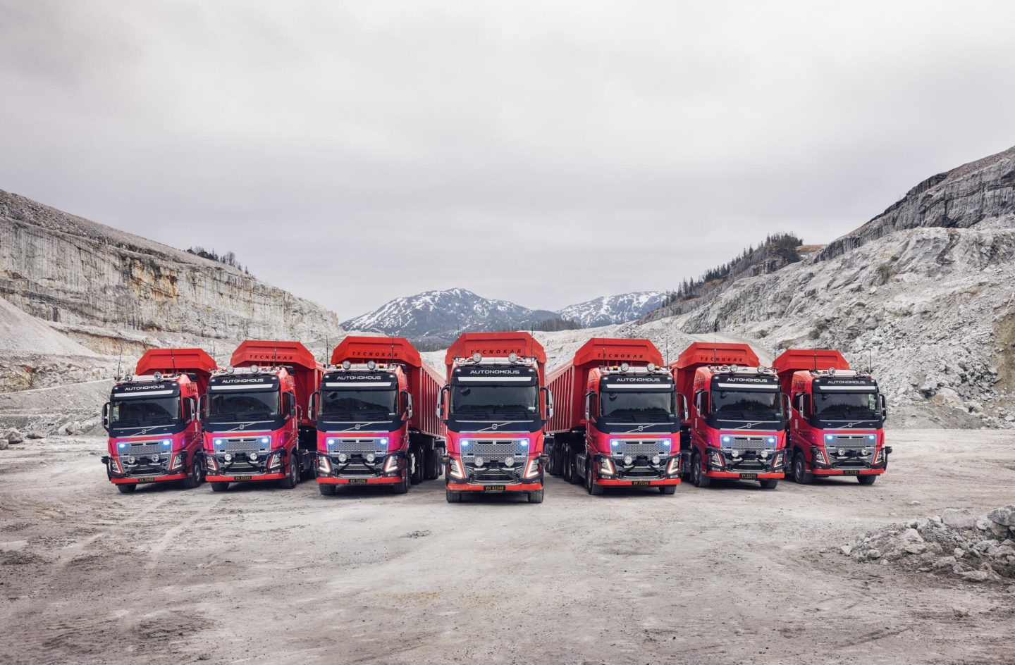 Range of 7 orange volvo autonomous trucks in a quarry