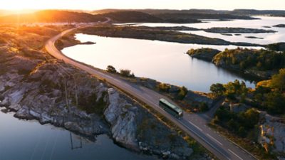 A Volvo electric coach driving along a coastal road at sunset, illustrating the transition toward more sustainable and decarbonized transport solutions.
