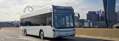 An articulated full hybrid bus drives alongside crops in a field