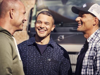 Een close-up van drie mannen lachend voor een Volvo-voertuig