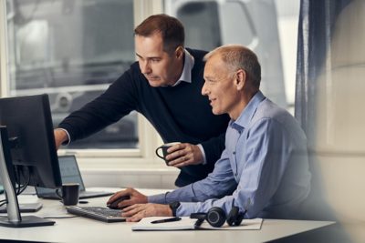 A man and woman stand in front of a truck looking at a tablet