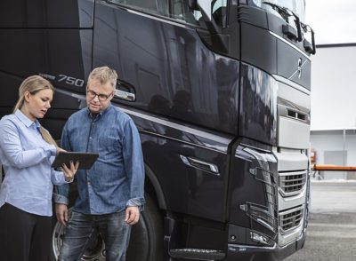 Um homem e uma mulher em frente de um camião a olhar para um tablet
