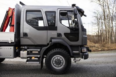 Samochód ciężarowy Volvo z szarą kabiną załogową pokazany z bliska z boku, zaparkowany na żwirowej powierzchni, z nagimi drzewami w tle.