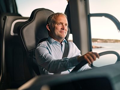 A smiling bus driver at the steering wheel of an electric Volvo coach