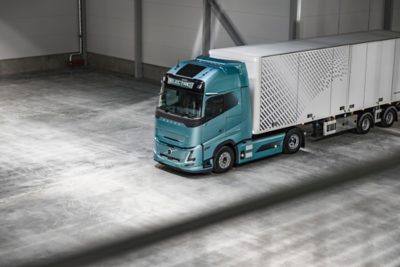 Elektrický nákladní automobil Volvo se skříňovým návěsem zachycený z nadhledu stojí zaparkovaný na leštěné betonové podlaze uvnitř velké průmyslové haly.
