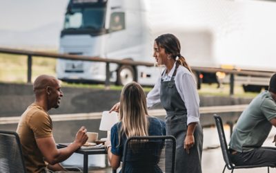 Oameni într-o cafenea, cu un camion Volvo în fundal