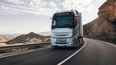 Ein Volvo FH fährt auf einer Autobahn durch eine felsige Landschaft mit Bergen und Wasser im Hintergrund