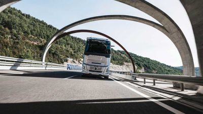 Ein Volvo FH fährt auf einer kurvigen Landstraße mit Felsen und Wasser im Hintergrund