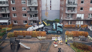 Koukkulaitteella varustettu sähkökäyttöinen Volvo-kuorma-auto, jonka kyydistä puretaan ECR25-konetta asuinalueella.