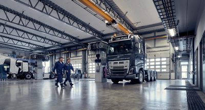 Volvo FH je zaparkované v dílně a před ním jdou dva mechanici Volvo.
