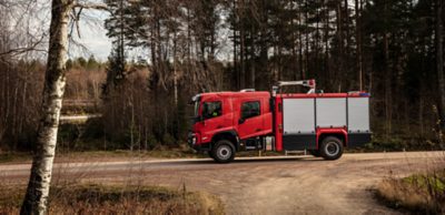 Czerwony wóz strażacki Volvo z kabiną stoi na żwirowej drodze na skraju lasu.