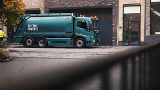 A Volvo electric refuse truck standing next to an entrance of a building.