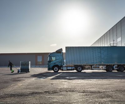 Camião Volvo FM a gás posicionado num local de logística enquanto um trabalhador manuseia a carga, demonstrando a eficiência nas operações de distribuição e transporte urbano.