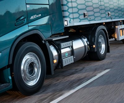 Grande plano do depósito de combustível GNL e das rodas traseiras de um camião Volvo FM movido a gás em movimento, destacando o design duradouro e o desempenho na estrada.