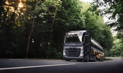 Samochód ciężarowy Volvo FM ciągnący błyszczącą przyczepę z cysterną po krętej leśnej drodze.