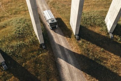 A Volvo FMX truck, viewed from above, navigates its way through a gravel road